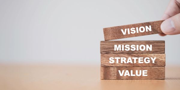 Wooden blocks labeled value, strategy, mission, and vision stacked, with a hand placing the vision block on top.