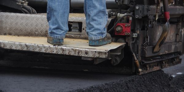 Worker standing on asphalt paving machine.