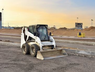 Skid-steer loader at a construction site at sunset.