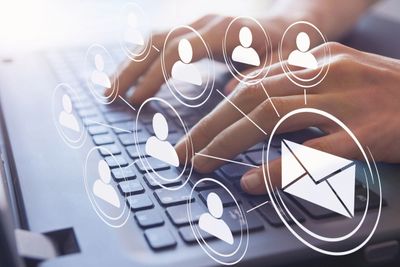 Person typing on laptop with digital icons of people and email symbol.