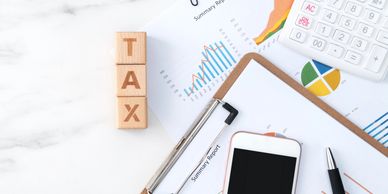 Tax blocks beside financial reports, calculator, clipboard, phone, and pen on a desk.