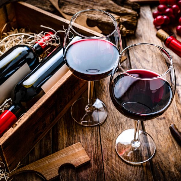 Two glasses of red wine next to wine bottles in a wooden crate.