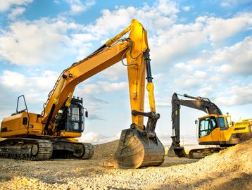 Two excavators parked on rocky ground under a blue sky.