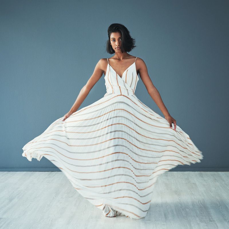 Shot of a beautiful young woman wearing a long flared dress against a blue background