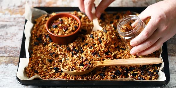 Hand scooping homemade granola into a jar with a wooden spoon.