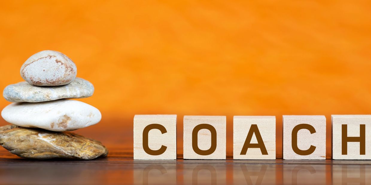 Stacked stones next to wooden blocks spelling "COACH" on an orange background.