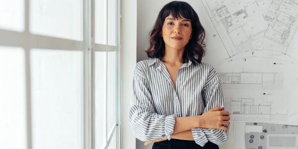 Confident woman standing with folded arms near architectural blueprints.