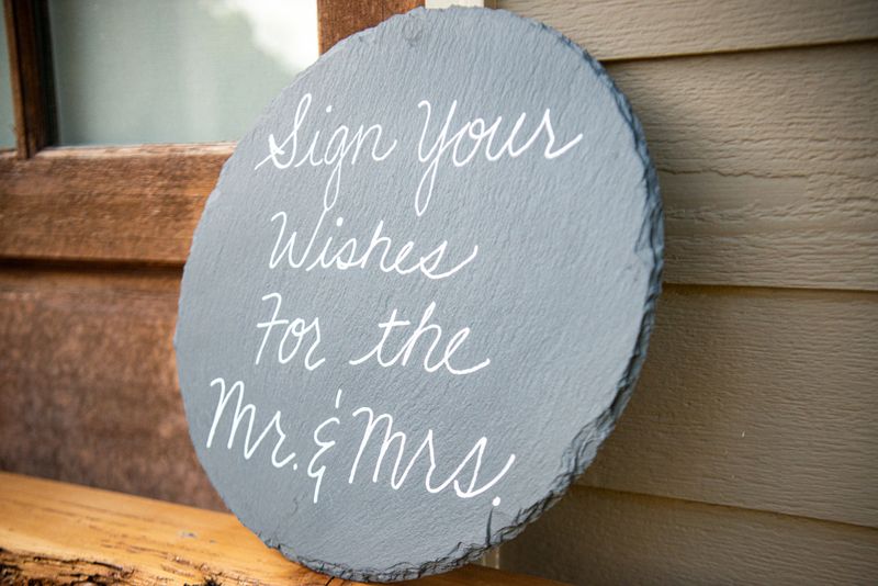 " Sign your wishes for the Mr. & Mrs. " grey slab sign with white lettersleaning on wall