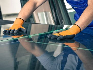 Worker wearing gloves handling large glass sheets carefully.
