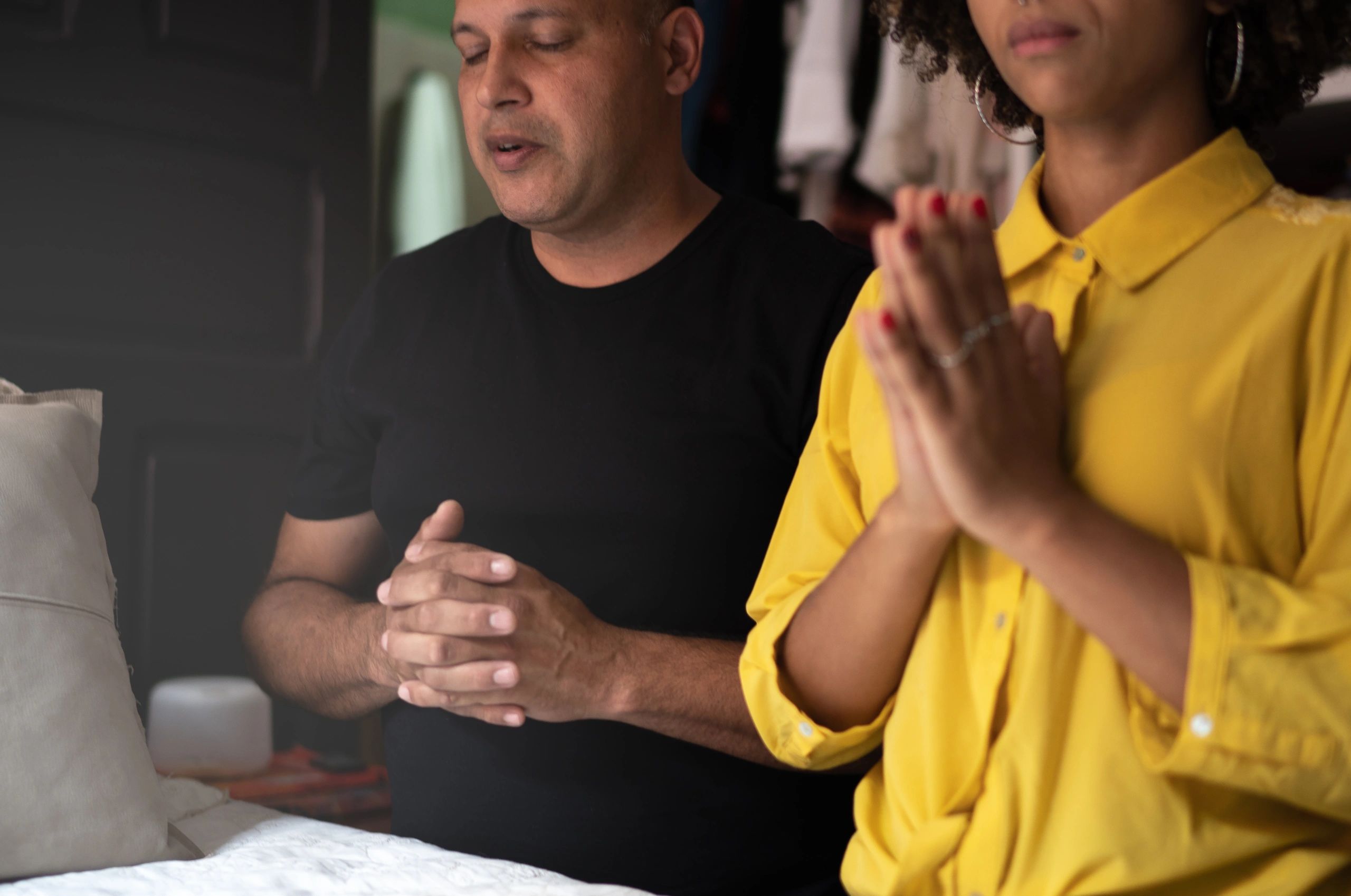 Two people praying with eyes closed and hands clasped together.