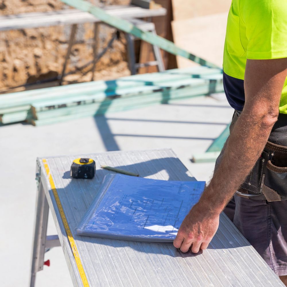 Construction worker reviewing blueprints on a worktable at a building site.