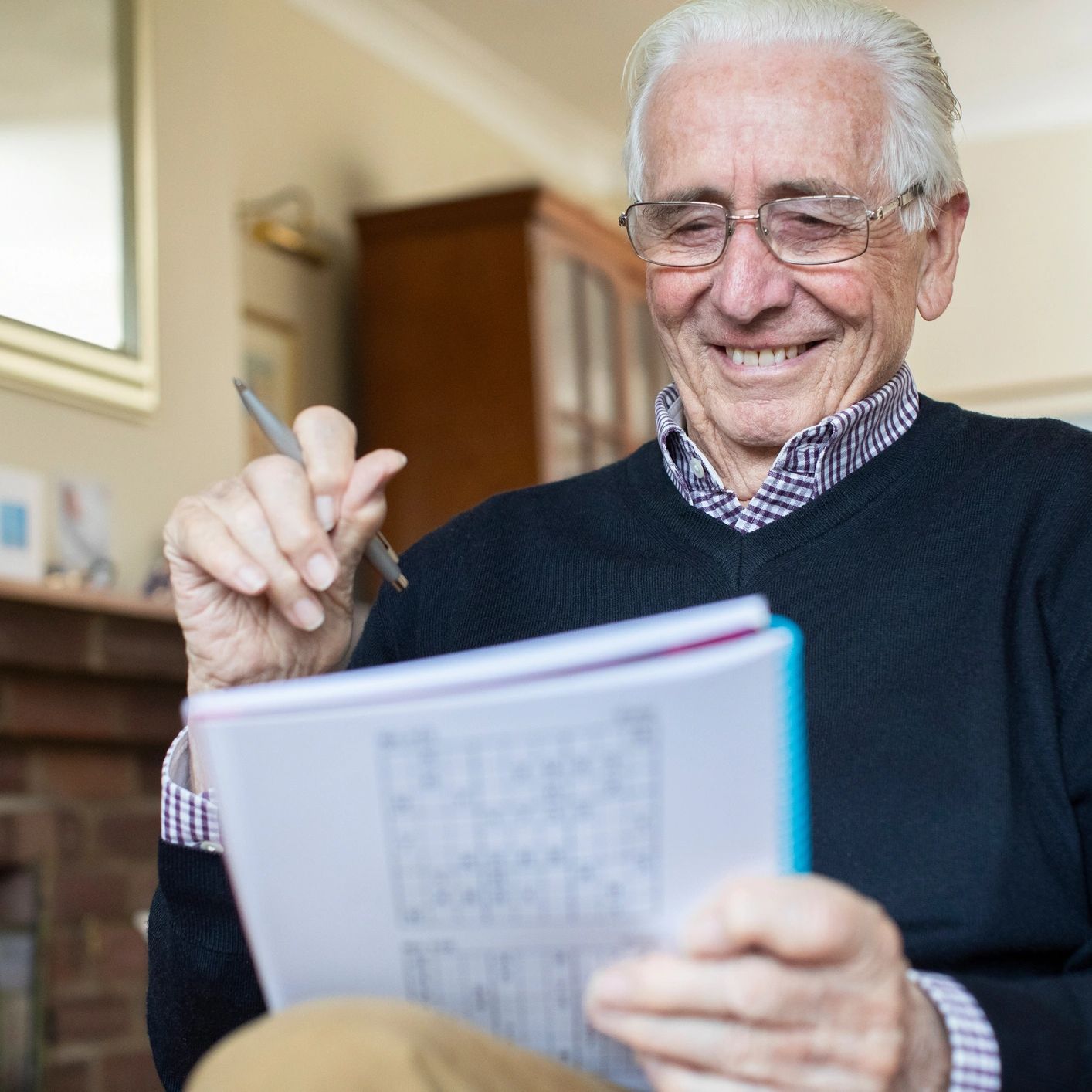 Smiling older man doing a crossword puzzle at home