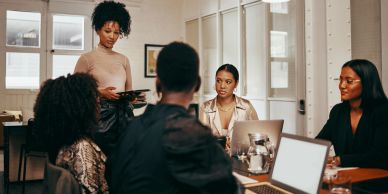 A woman stands and speaks to colleagues in a modern office meeting.