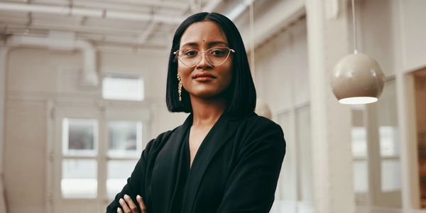 Confident woman in black blazer with glasses standing in office.