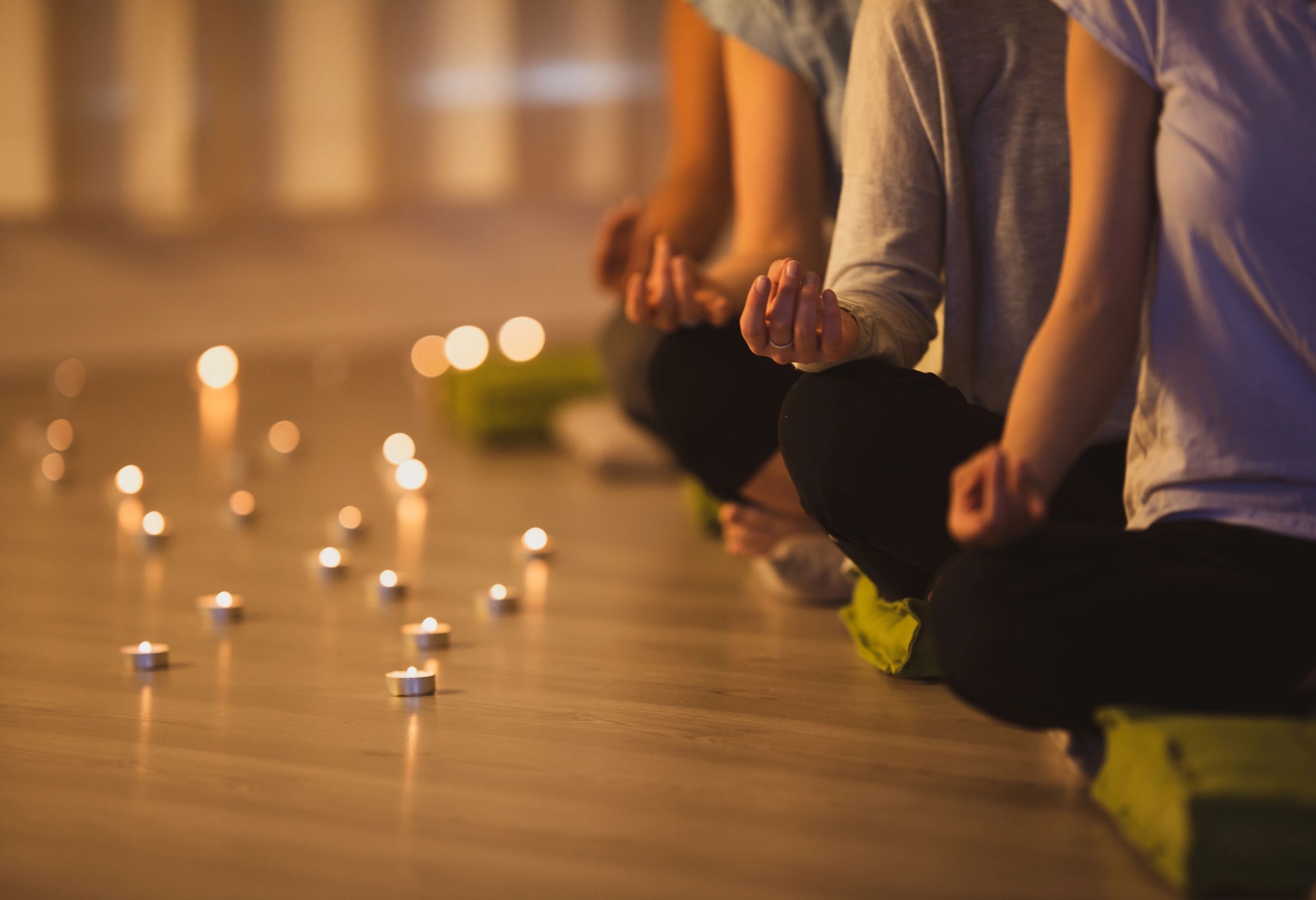 People meditating with candles lit around them in a calm setting.