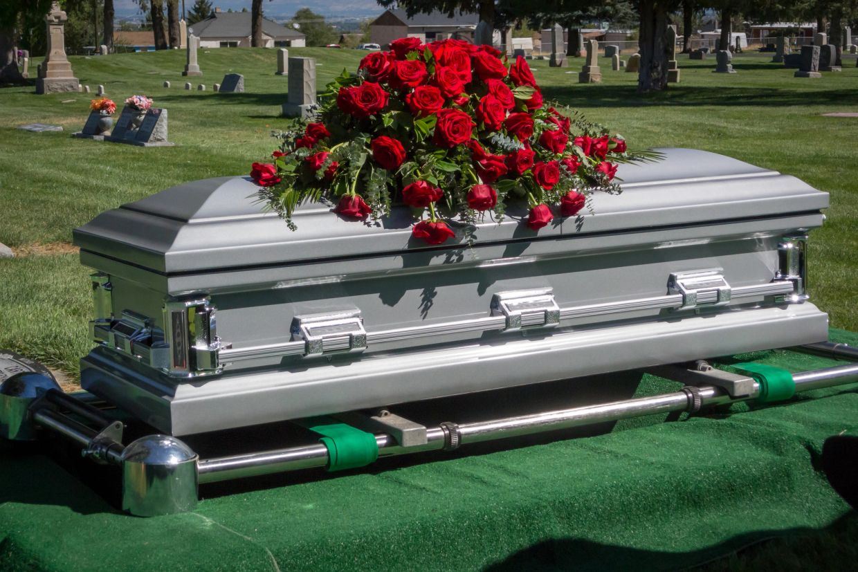 Silver casket with red roses at a cemetery.