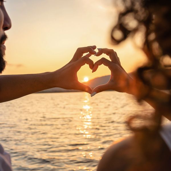 Couple forming a heart with hands at sunset by the water.