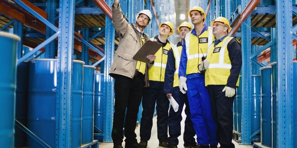 Warehouse workers in safety gear inspecting inventory in a large storage facility.