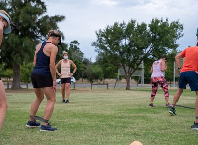 Group exercising outdoors with resistance bands on legs.