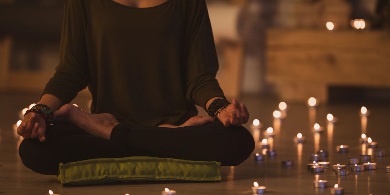 Person meditating surrounded by candles.