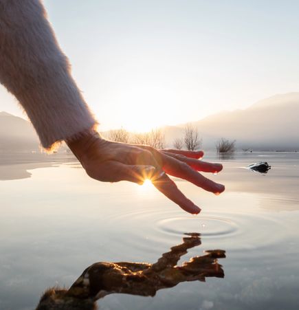 Hand touching calm water at sunrise.