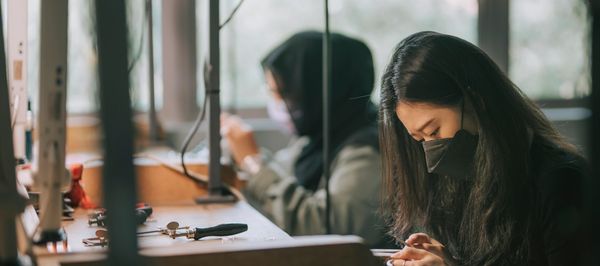 Two women wearing masks focused on crafting at workstations.