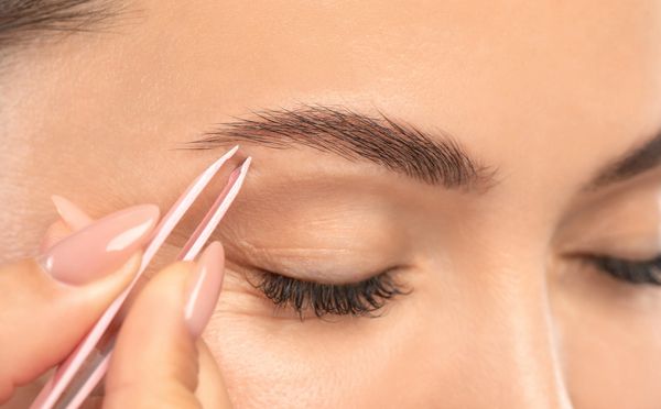 Persona depilando cejas con pinzas.