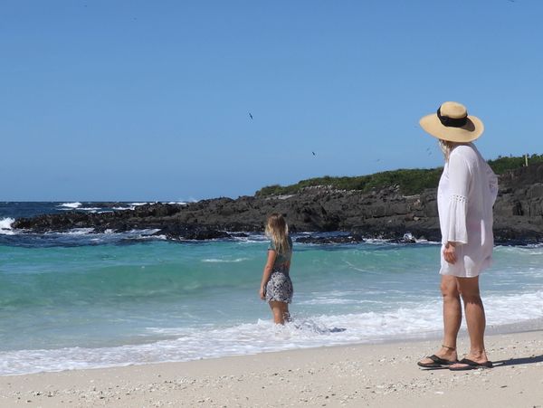 Two women enjoying a sunny day at a rocky beach with clear blue skies.