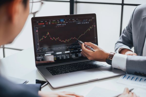Two professionals analyze stock market trends on a laptop screen.