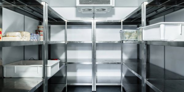 Empty industrial refrigerator with metal shelves and few food items.