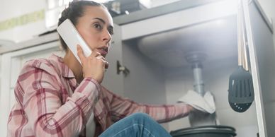 Woman on phone fixing a kitchen sink under the counter.