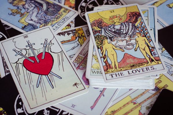 Tarot Cards in a messy pile. On top are "The Lovers" card and the other has a red heart & 3 swords.