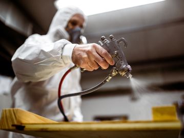 Person spray painting a wooden surface wearing protective gear.
