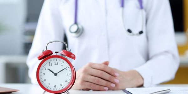 Doctor with a stethoscope and a red alarm clock on the desk.