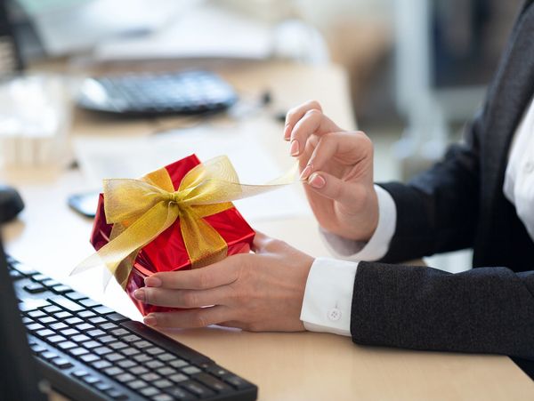 Person at desk opening a red gift with a gold ribbon, representing thoughtful corporate gifts.