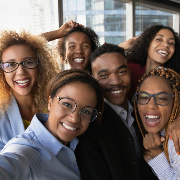 Group of six happy young adults taking a selfie indoors.