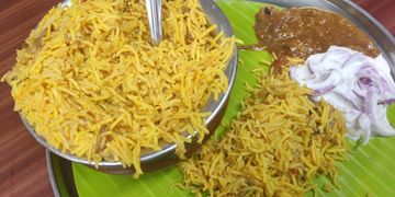 A plate of biryani served with raita and curry on a banana leaf.