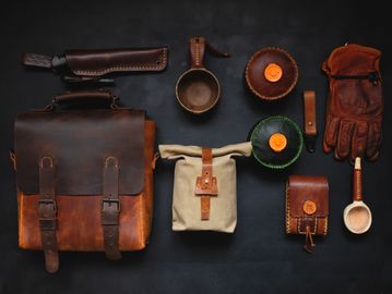 Rustic leather and canvas outdoor gear neatly arranged on black background.