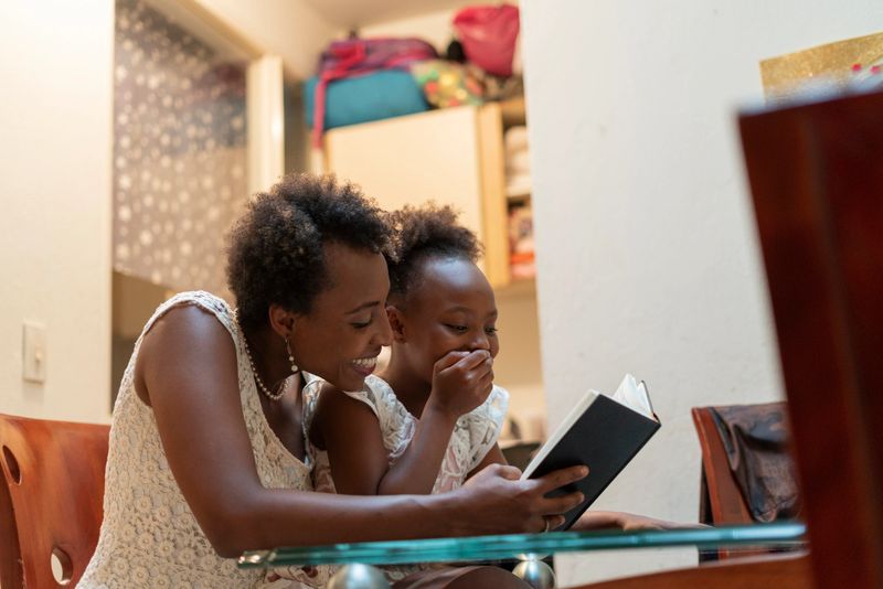 Latin mother from Bogota Colombia between 20 and 29 years old, reads a beautiful book to her 7-year-old daughter in the tranquility of her home while the two enjoy the moment during the COVID 19 quarantine