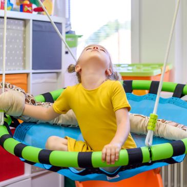 Child playing on a colorful swing indoors.