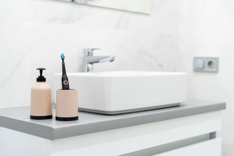 Oral care and dental hygiene concept. Electric toothbrush in cup and soap dispenser bottle near basin. Element of white modern bathroom with chrome water tap over sink at blurred copy space background
