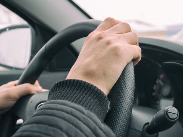 Person holding a car steering wheel while driving.