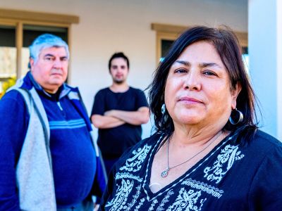 Three individuals standing outside a building, looking serious.