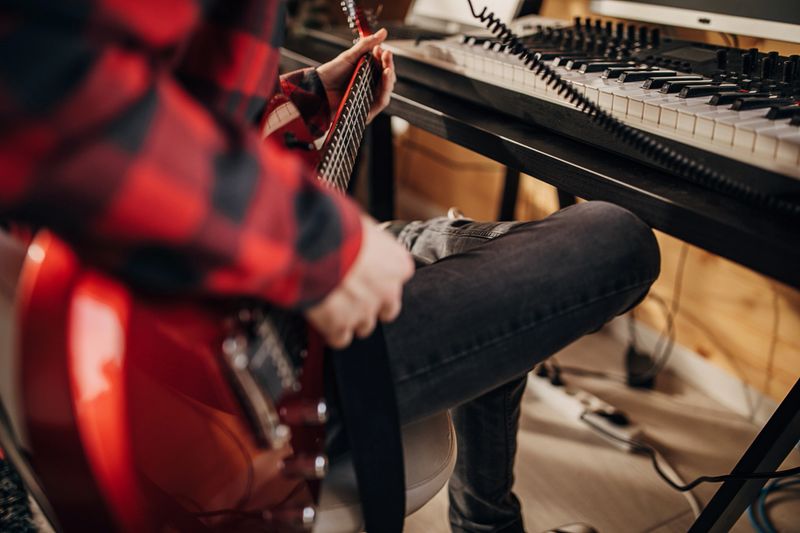 One man, teenage male guitarist playing electric guitar in recording studio at home.