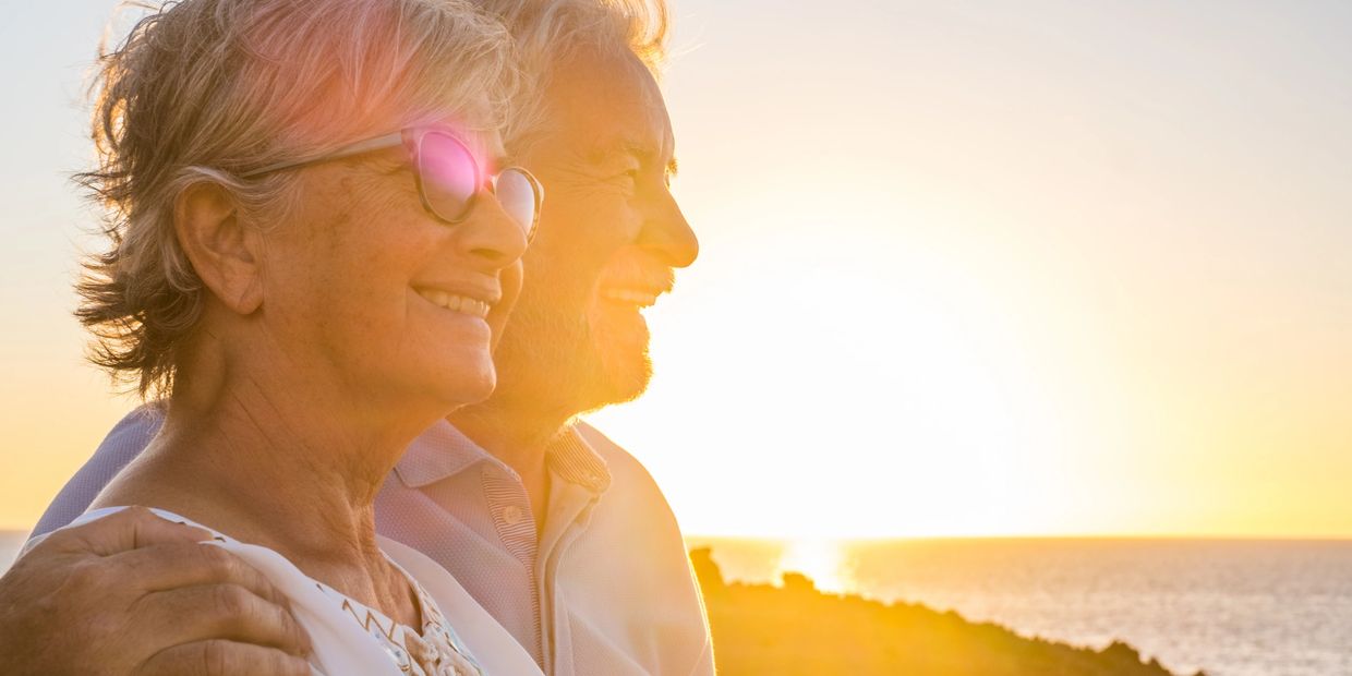 an elderly couple standing together in front of the sun