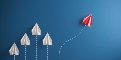 A red paper airplane diverging from a group of white paper airplanes on a blue background.