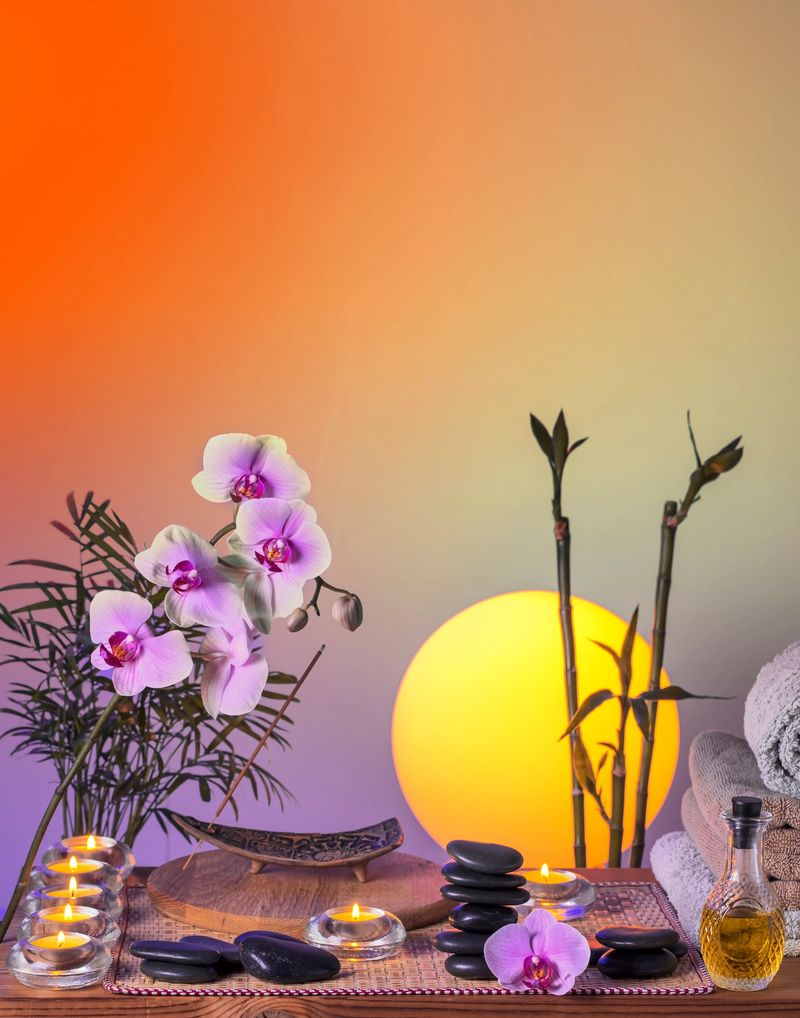 Black massage (balance) stones, Orchid flowers, bamboo plant, incense stick, towels, candles and massage oil on a wooden table. Evening sun at the background. Space for copy.