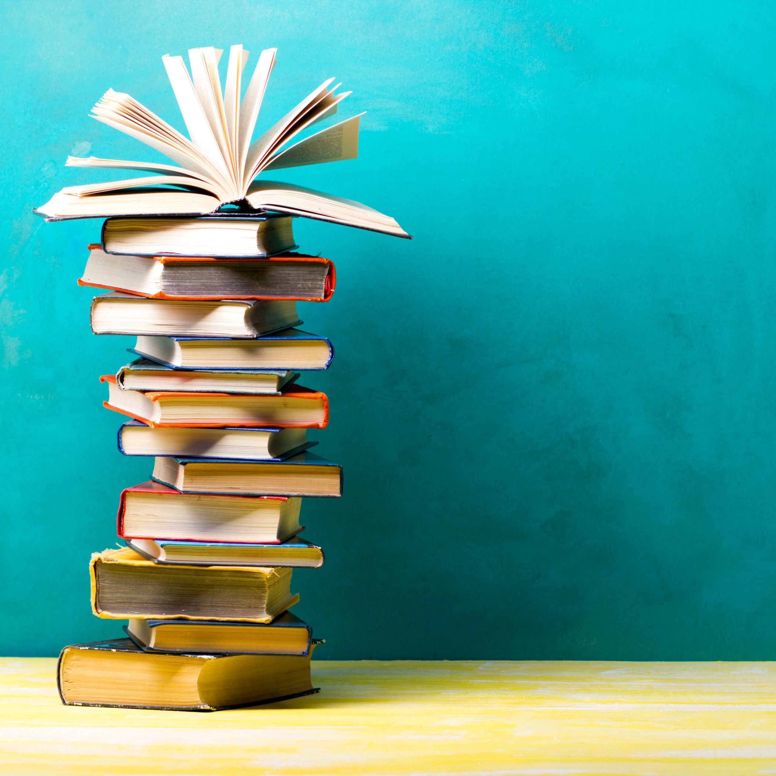 Stack of books with one open book on top against a turquoise background.