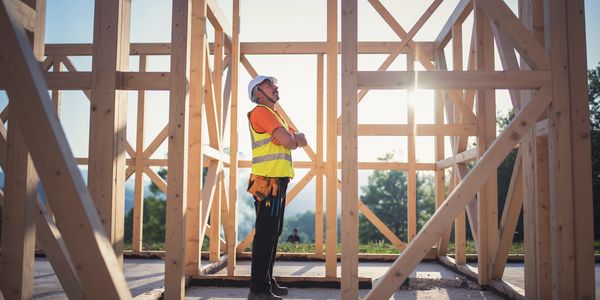 Construction worker inspecting wooden frame structure at sunrise.