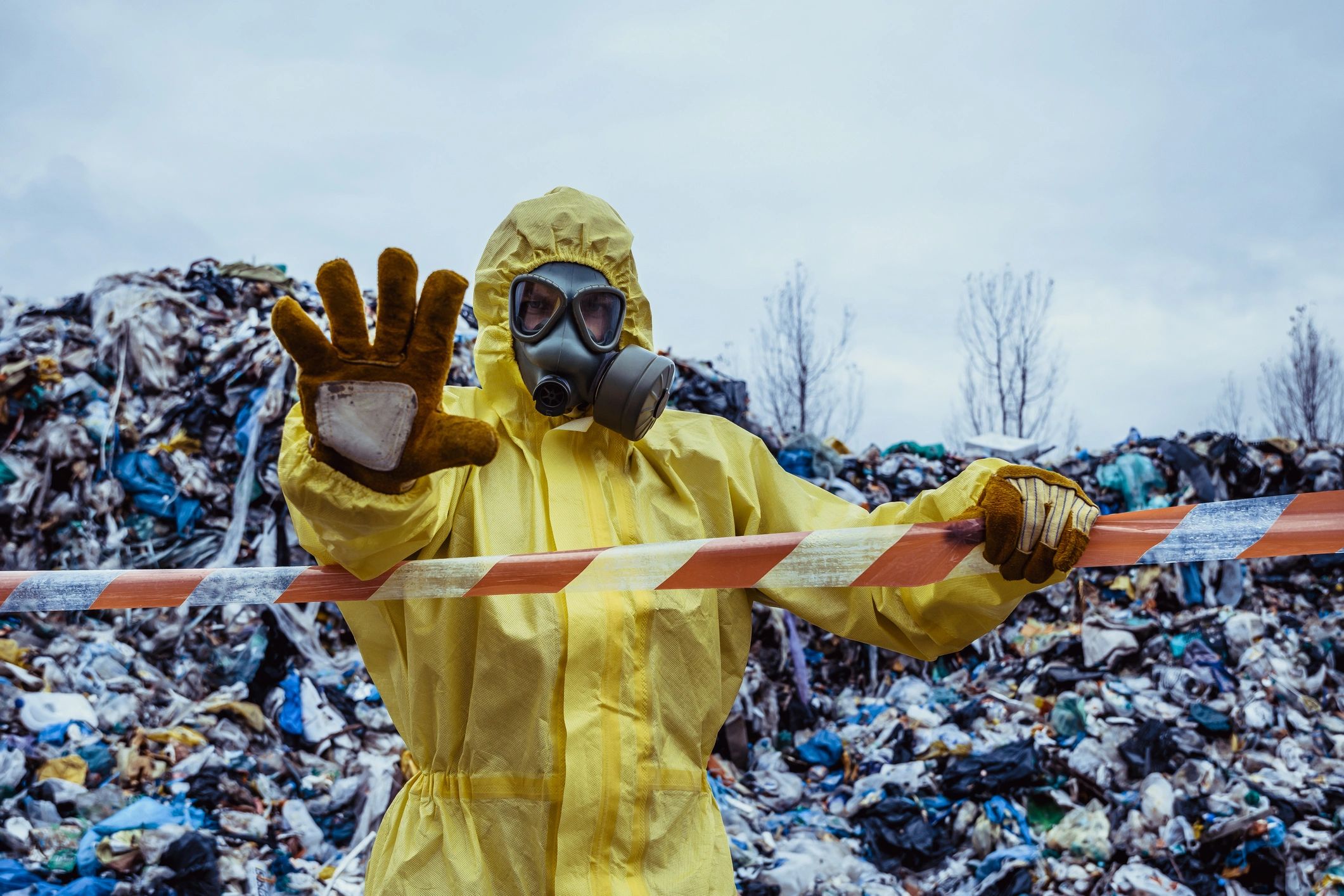 Person in protective gear and gas mask at a waste disposal site.